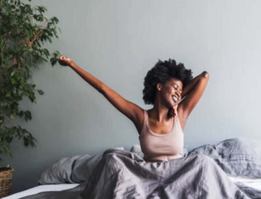 Woman stretching and smiling in bed, promoting sleep coach training programs.